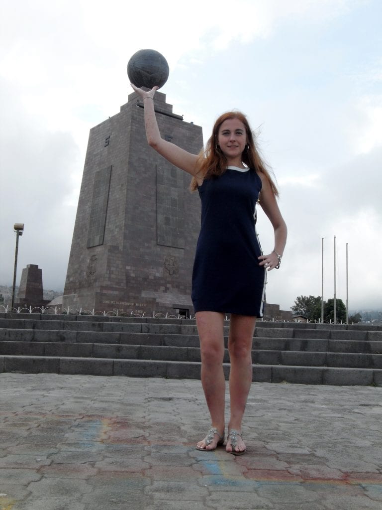 A woman holds up the ball on top of the equator monument, a popular activity in Ecuador 