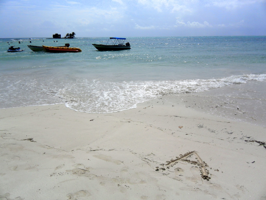 Crystal-clear waters gently wash up on the white sandy beach of San Andres Island with boats and a water scooter moored in the distance, highlighting a serene tropical paradise perfect for water sports and relaxation.