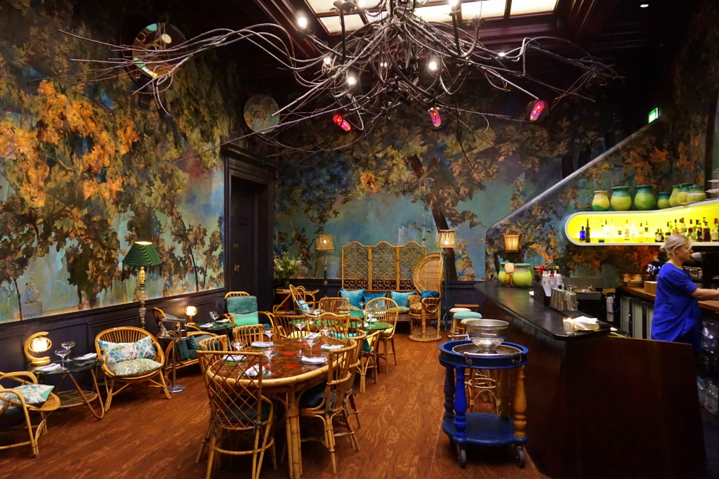 Eclectic interior of a London cafe with whimsical decor and a forest-inspired mural, reflecting the unique dining experiences available in the city, a cozy spot for visitors to unwind after sightseeing.