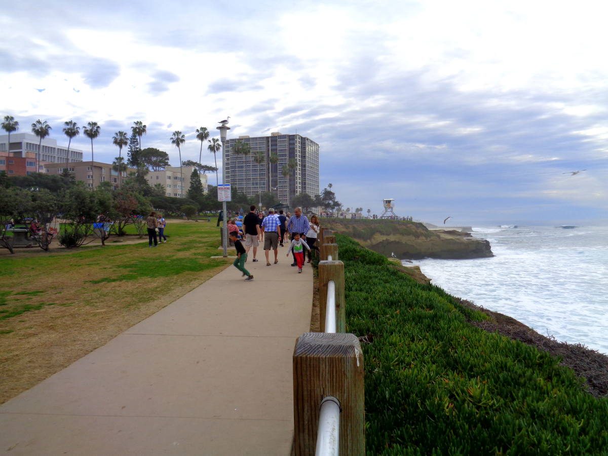 People strolling along a scenic coastal path with lush greenery on one side and the ocean on the other, ideal for traveling in the US with a baby.