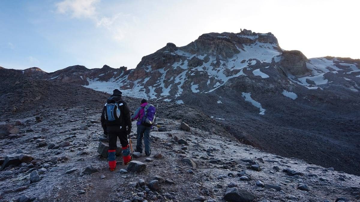 Two people dressed in warm clothes hiking up a wet rocky slope of Cotopaxi Volcano.