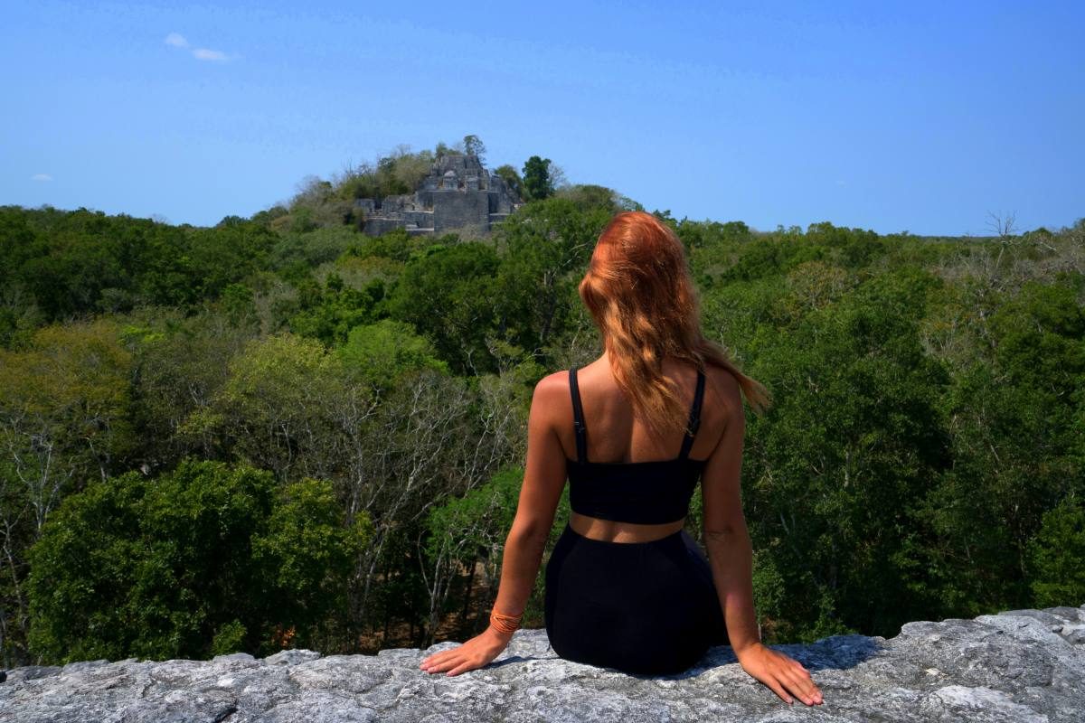 A solitary figure overlooking ancient Mayan ruins nestled in the dense jungle, representing the historical allure of unique places in Mexico.
