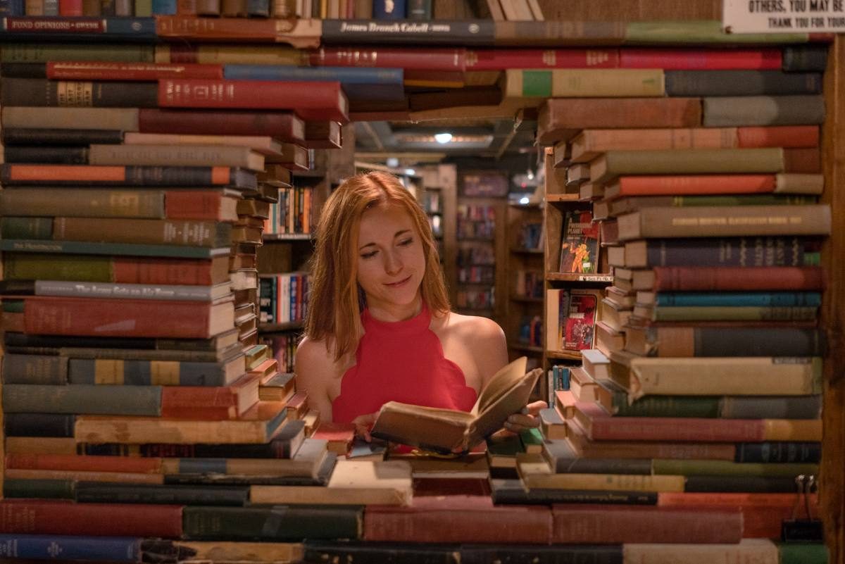 Woman reading a Spanish book in a cozy bookstore surrounded by towering stacks of books, immersing herself in the language.
