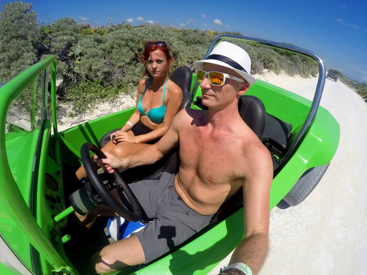 Couple riding in a bright green dune buggy rental on a sandy path in Mexico, embracing the adventurous side of renting a car in Cozumel