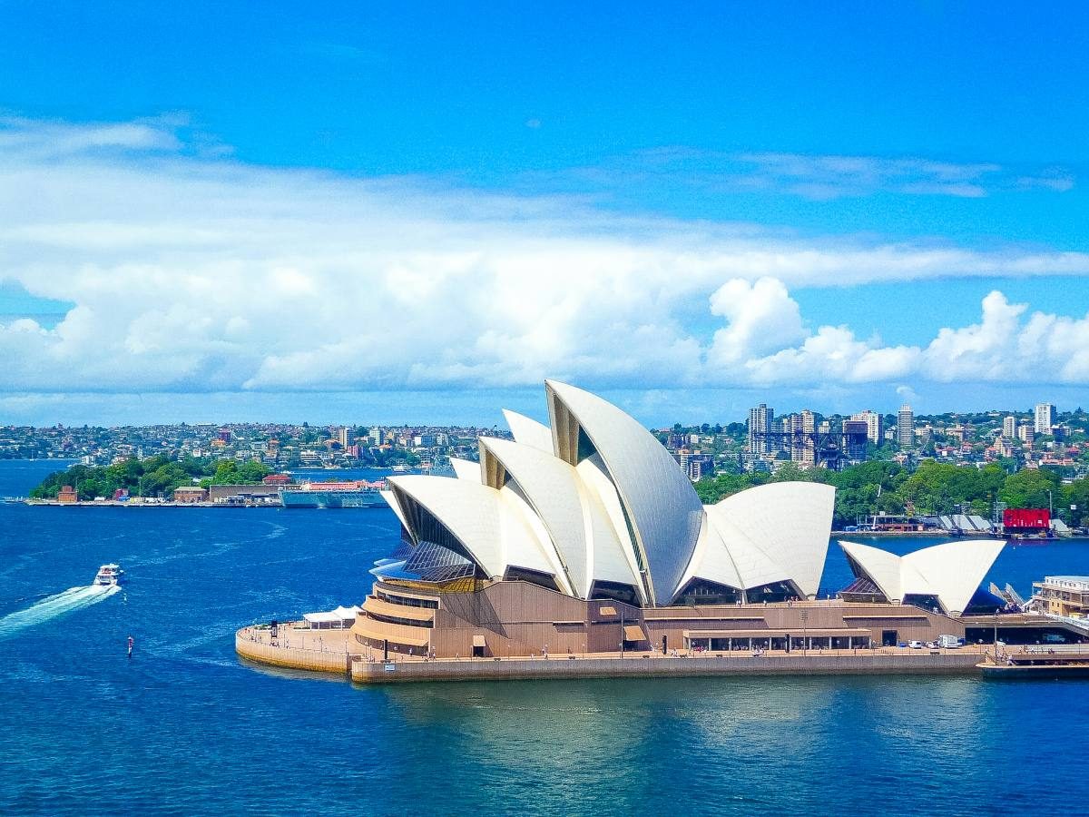 The iconic Sydney Opera House stands majestically against a blue sky, with Sydney Harbour bustling with activity, capturing the essence of moving to Sydney, Australia.