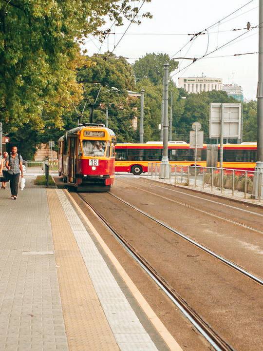 Classic tram passing through a lush green avenue in Warsaw, part of the convenient public transport system for residents living in Poland.
