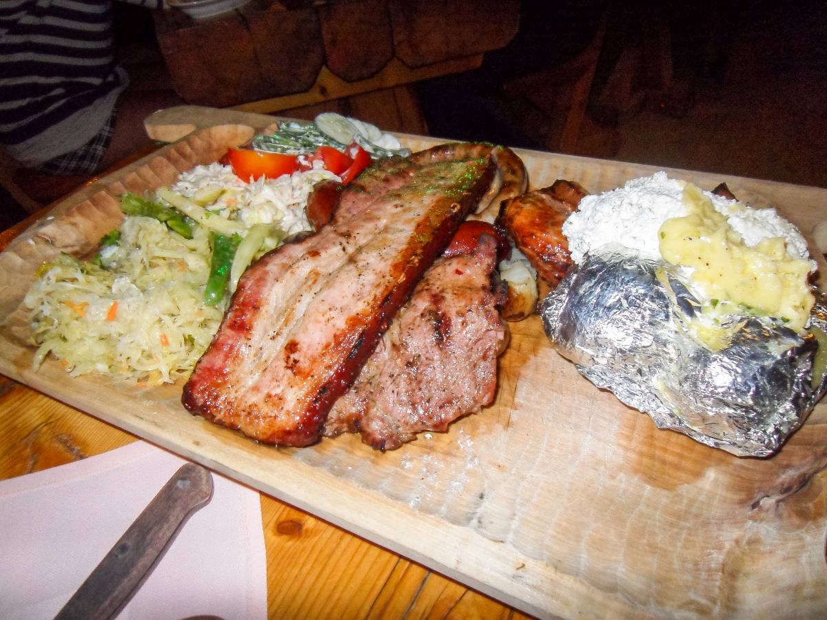 Wooden platter with an assortment of Polish grilled meats, including kielbasa and pork ribs, served with sauerkraut and baked potato, epitomizing the traditional Polish food.