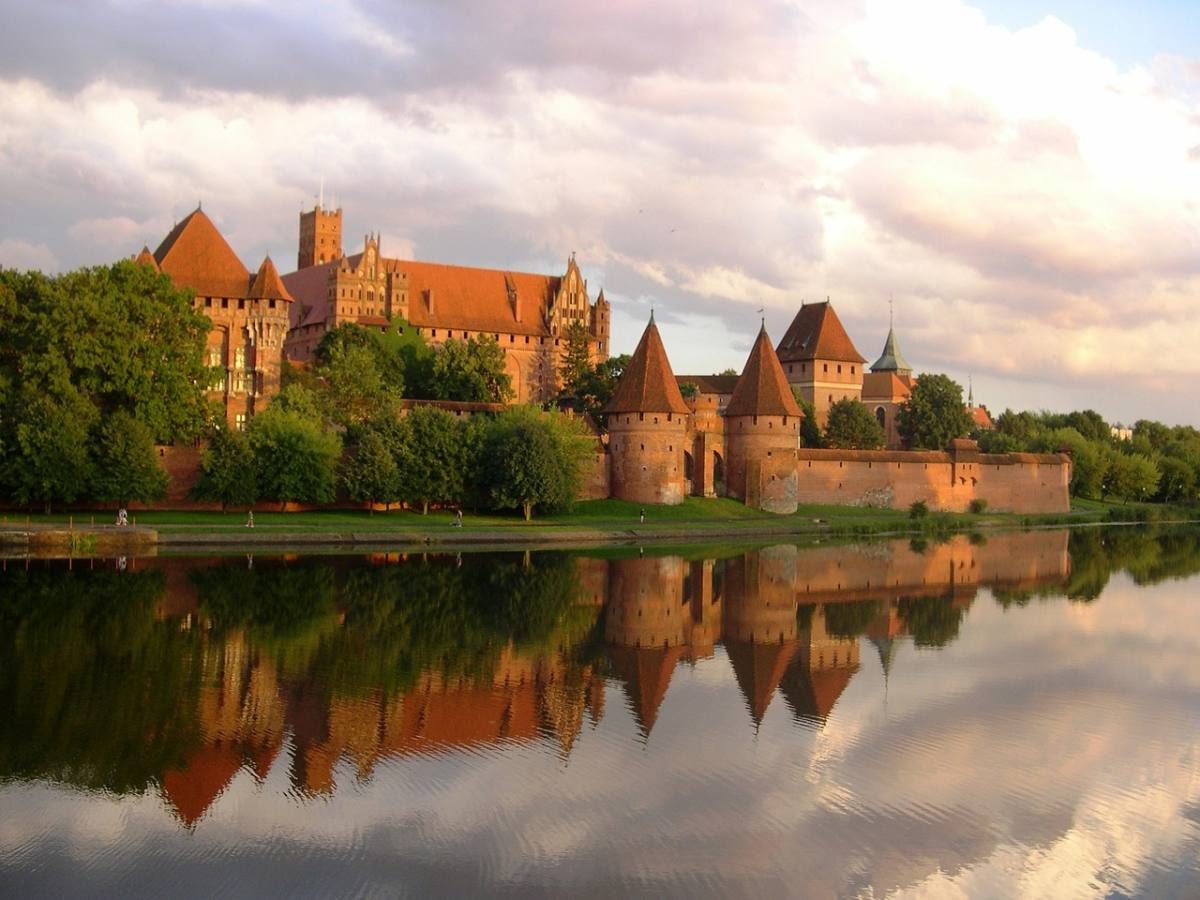 The majestic Malbork Castle reflected in the calm waters around it, representing Poland's historical and architectural grandeur.
