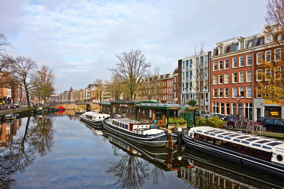 Serene view of Amsterdam's canal houses and houseboats, reflecting a calm morning in a city area where one might choose to stay.
