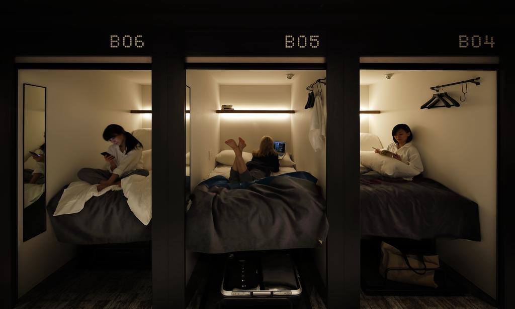 Capsule hotel experience in Tokyo with guests using smartphones in cozy pods.
