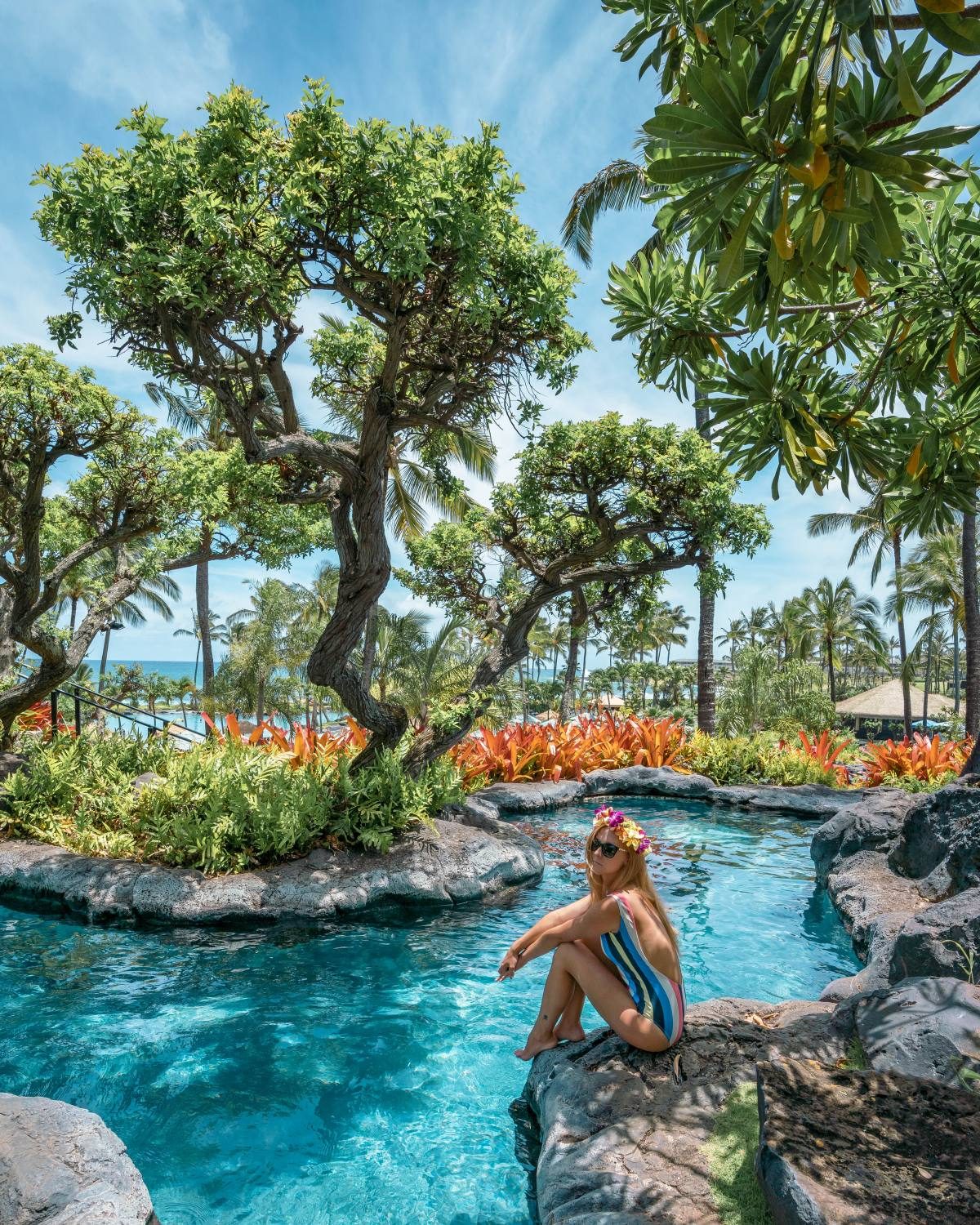 Wearing a striped multi-colored swimsuit sitting next to a rock pool.