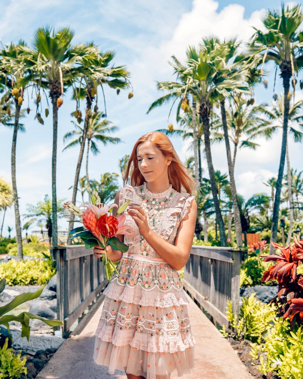 Lady in flowery dress holding a bunch of flowers.