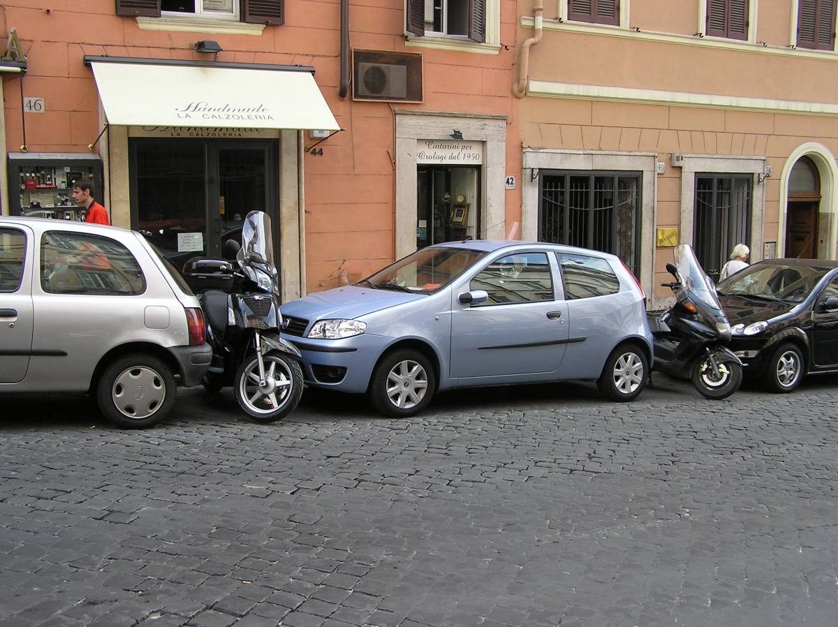 Compact car squeezed into a tight parking spot on a cobblestone street, showing the practical side of renting a car in Italy's urban areas.
