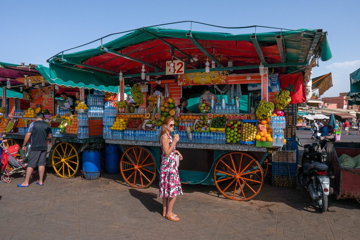 Marrakesh A traveler enjoying a fresh fruit juice from a vibrant market stall in Marrakech, a refreshing tip for any Marrakech travel guide.
