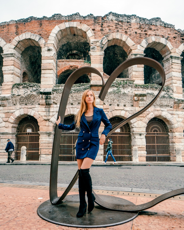 Stylish woman posing with a modern sculpture in Piazza Bra, Verona, blending contemporary art with the city's historic backdrop.