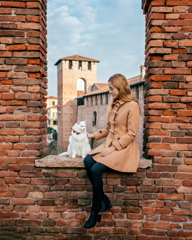 Woman with a white cat sitting on the ancient walls of Castelvecchio Verona , a city rich with history and perfect spots for memorable photos.
