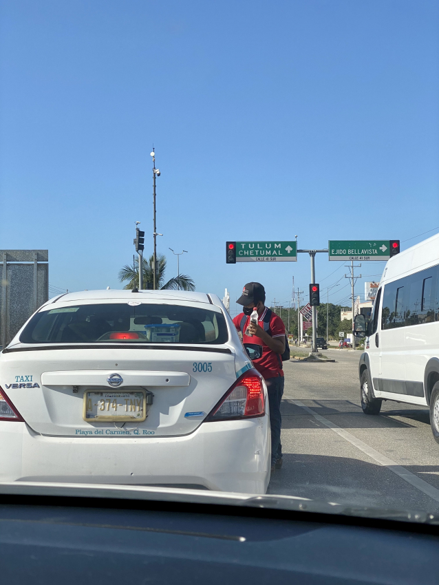 A local street vendor approaching cars at a traffic stop in Mexico, an experience often encountered when renting a car for city travel.
