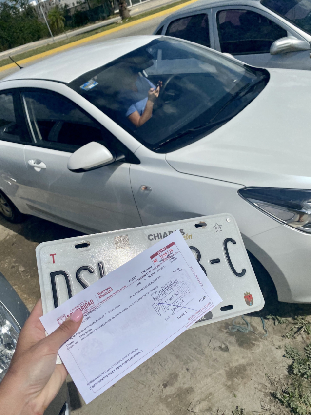 Hand holding a parking ticket next to a car with a Mexican license plate
