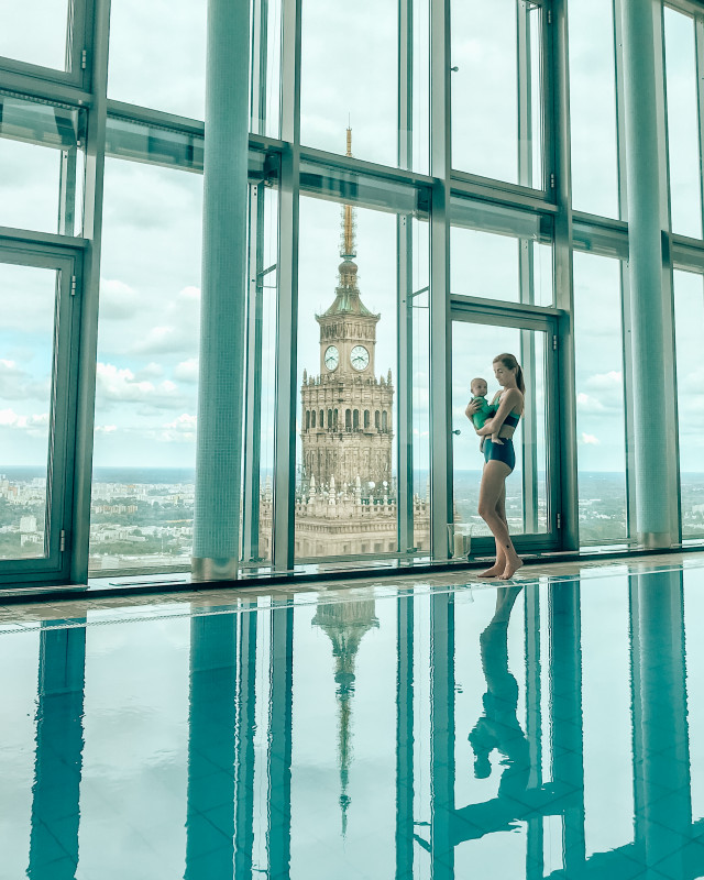 Woman with a baby enjoying the view from a high-rise pool with Palace of Culture in the background, a prime location in Warsaw.
