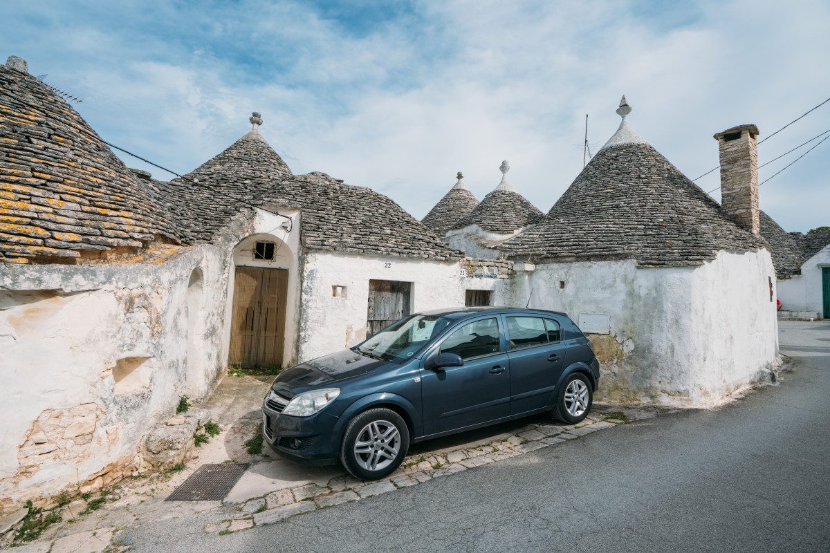 Blue car parked in front of unique trulli houses, a perfect example of renting a car in Italy to explore quaint village