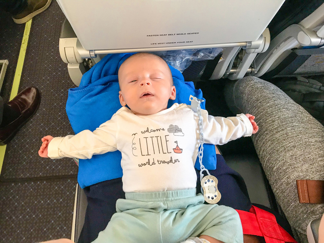 Infant sprawled out asleep on an airplane seat, demonstrating the makeshift comfort while flying with an infant on lap.
