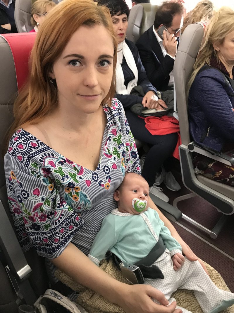 Young mother holding her infant during a flight, highlighting the care needed when flying with a baby.
