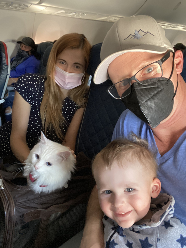 Family selfie on an airplane, with a toddler and a fluffy white cat, showing how to keep a 1-year-old entertained on a flight