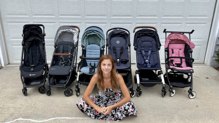 Woman sitting cross-legged in front of a lineup of various best travel strollers, smiling at the camera.
