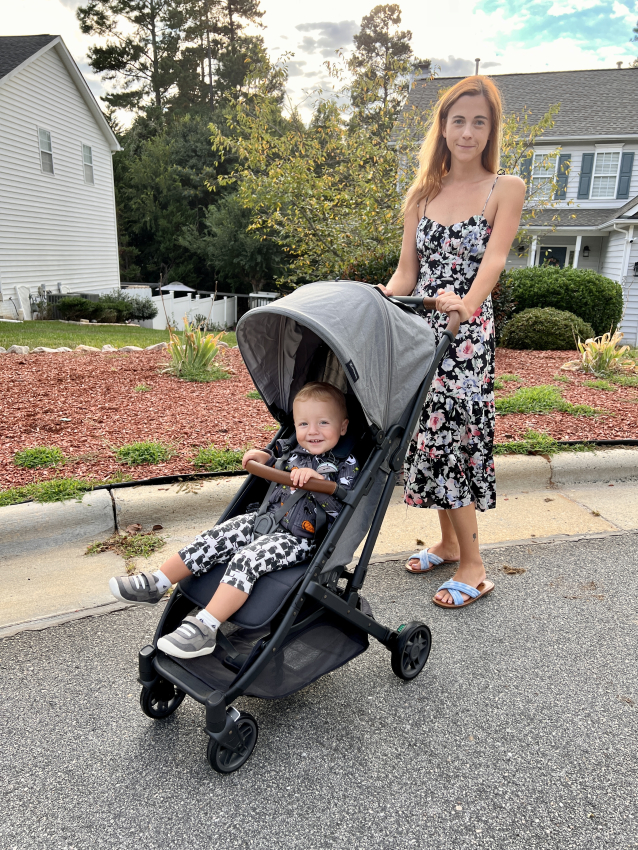 Woman in a floral dress pushing a grey travel stroller, blending style and convenience for active parents.