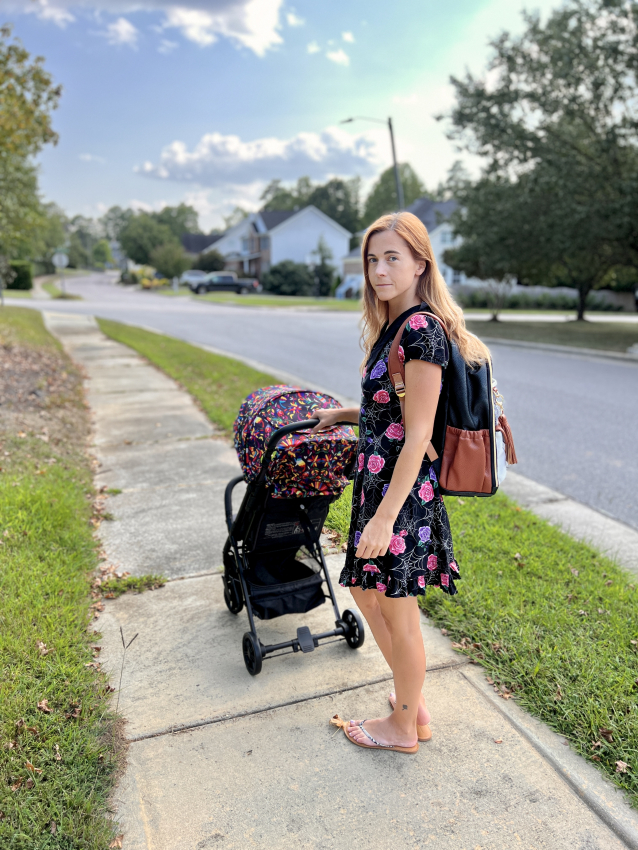 Woman with a patterned travel stroller on a suburban sidewalk, illustrating the everyday practicality of a compact stroller.