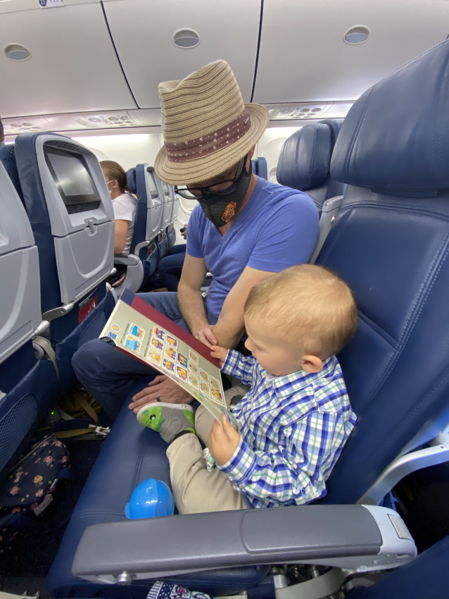 Dad reading a book to his toddler on a flight, a calming activity for flying with a toddler.
