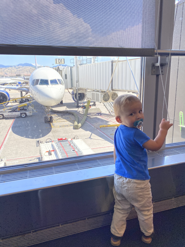 Curious toddler looking out at an airplane from the airport window, an exciting part of flying with a toddler.
