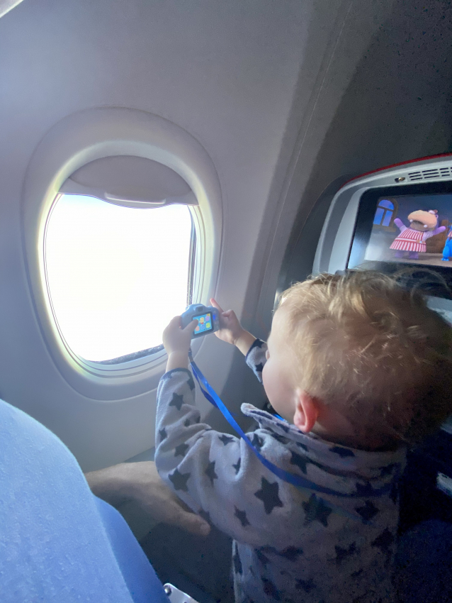 Engrossed toddler taking photos out of the airplane window, a great way to capture memories and keep a young traveler engaged on a flight.