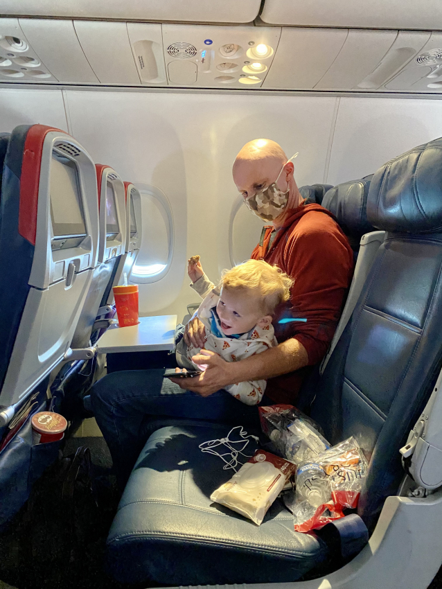 Father and toddler enjoying a snack on an airplane, sharing a moment while flying with a toddler.