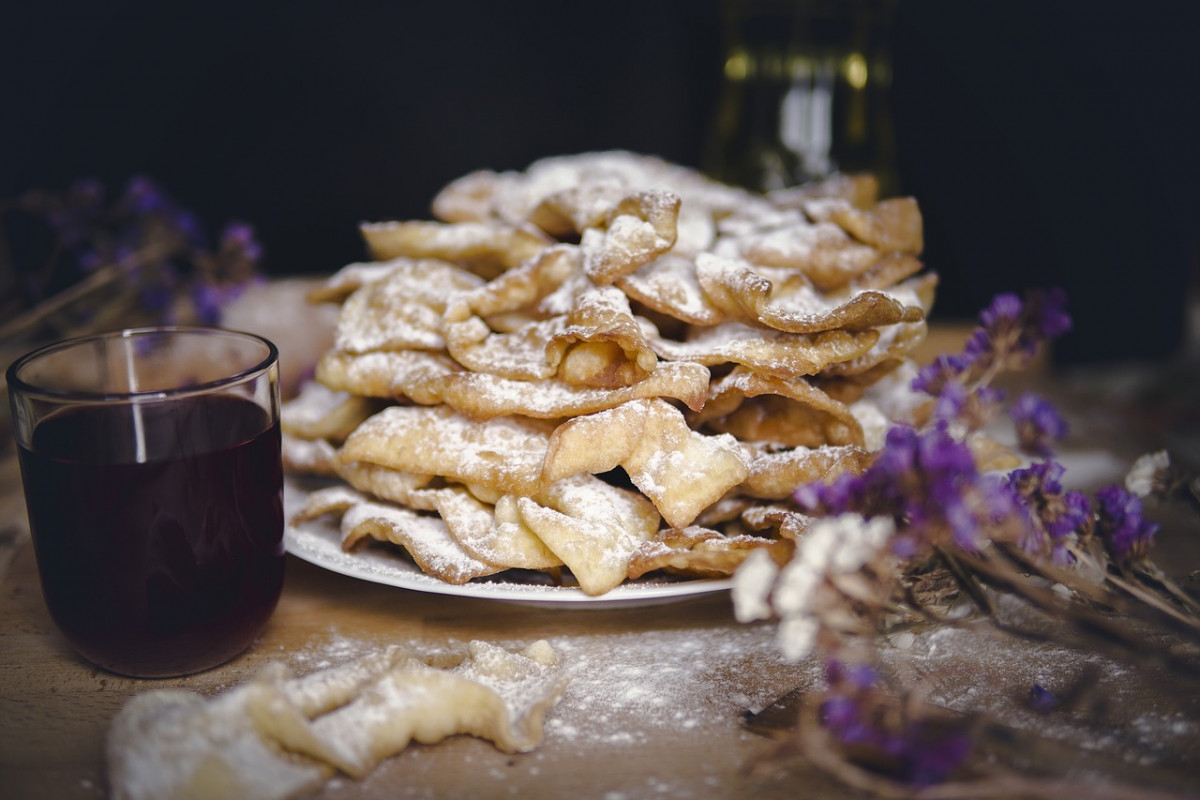 Stack of crispy Polish Angel Wings, or faworki, dusted with powdered sugar, alongside a glass of red compote, encapsulating traditional Polish desserts