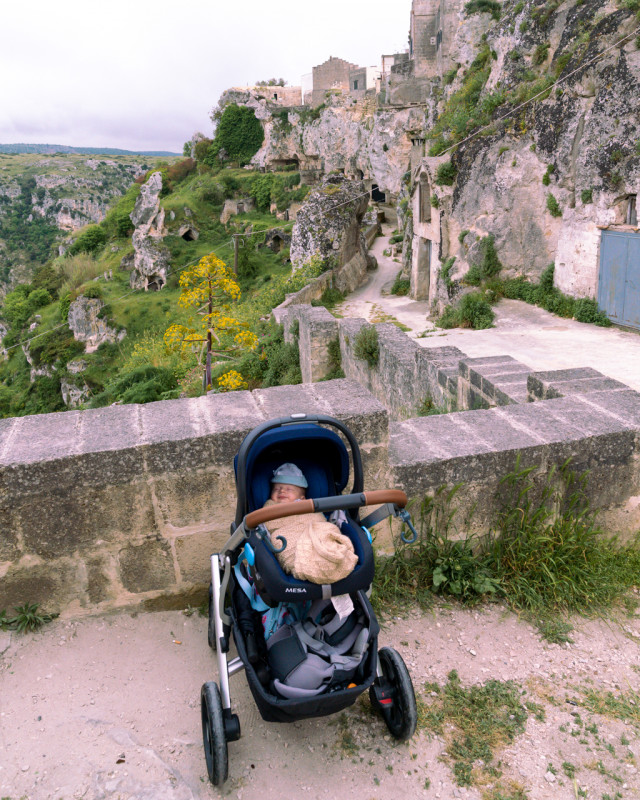 Baby in a stroller by the ancient stone steps in Matera, blending the old-world charm of Italy with modern family travel.