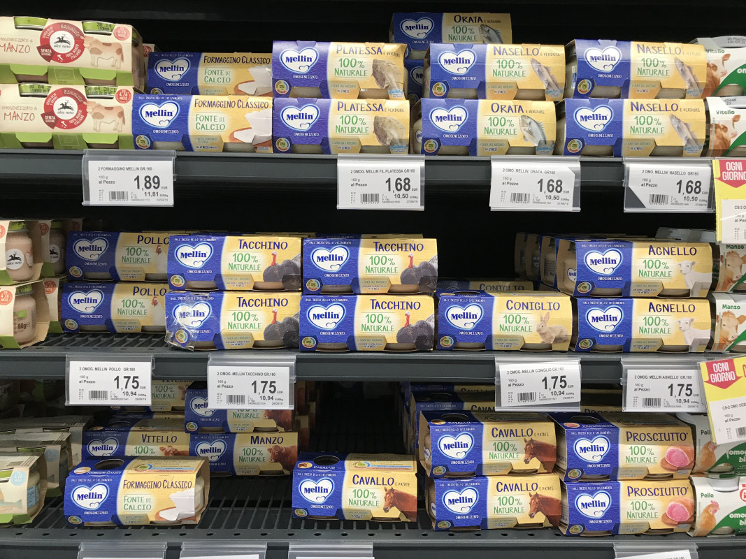 A neatly organized Italian grocery store shelf fully stocked with various baby foods, showcasing options baby food in Italy.