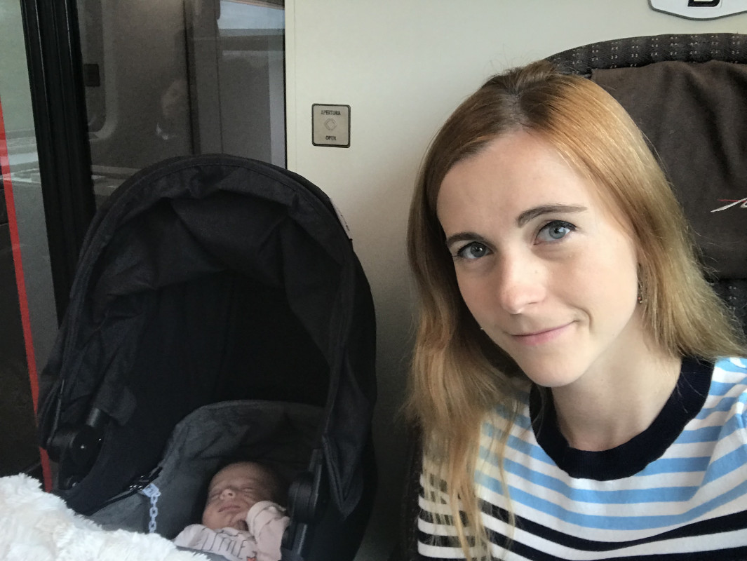 Mother taking a selfie with her sleeping baby in a stroller aboard a train, illustrating the practicalities of traveling through Italy with a baby.