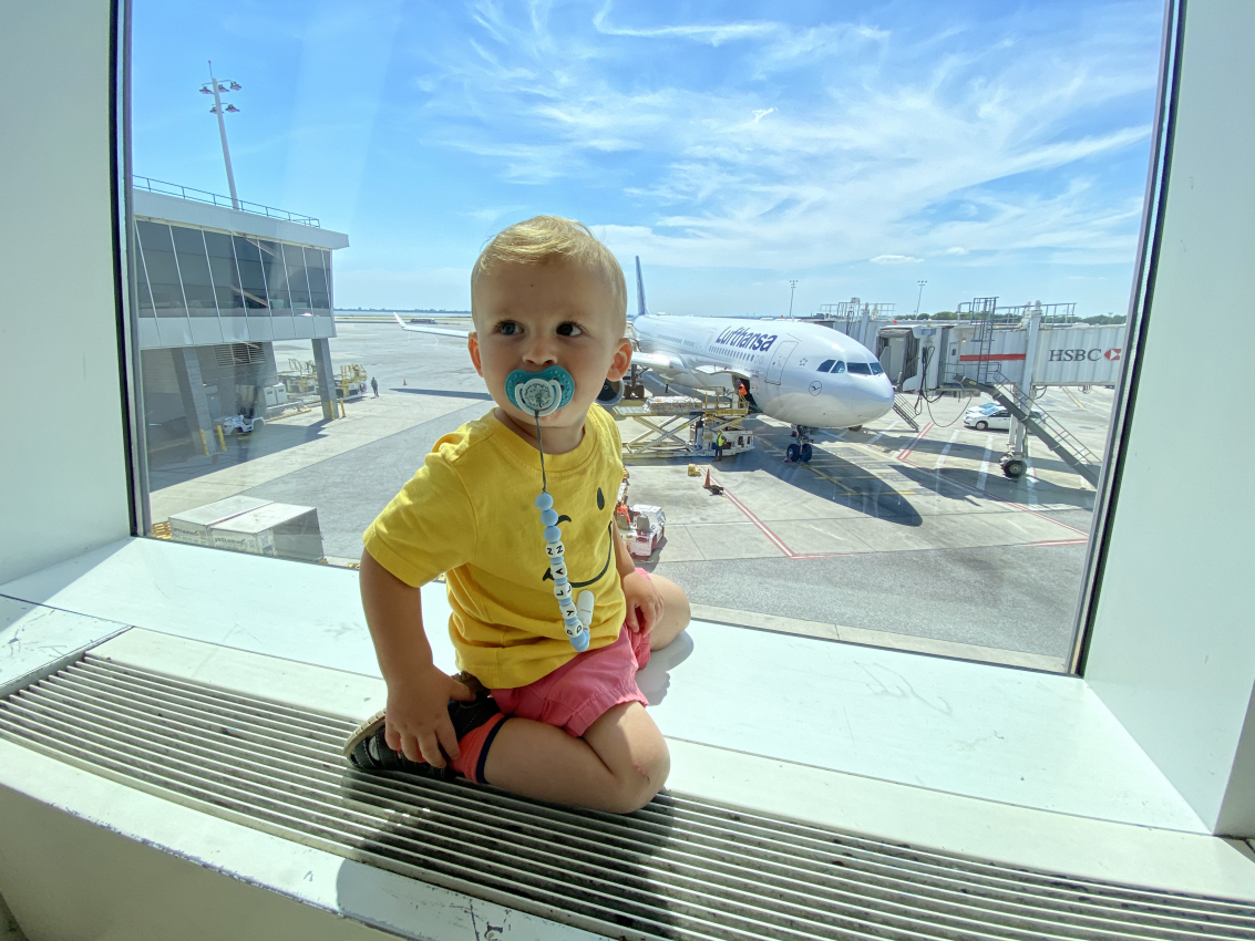 Young toddler sitting at the airport gate, watching planes, a perfect activity when flying with a toddler.
