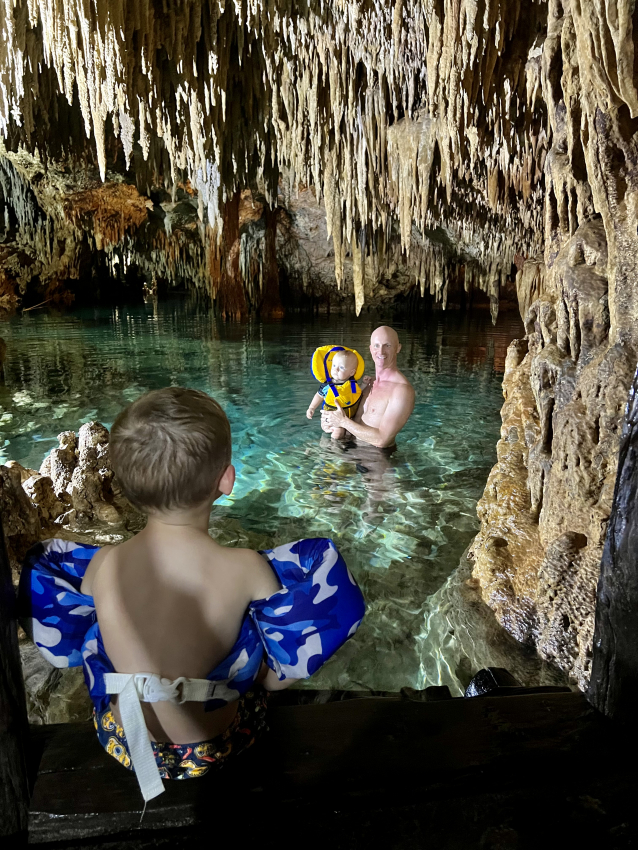 Toddler captivated by the sight of his father holding a baby in Mexico's enchanting cenote waters.