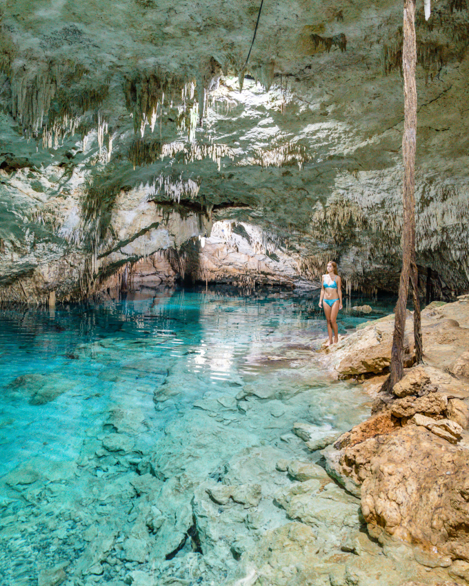 A woman contemplates the clear blue waters of a serene cenote, one of the many unique places in Mexico known for their natural beauty.