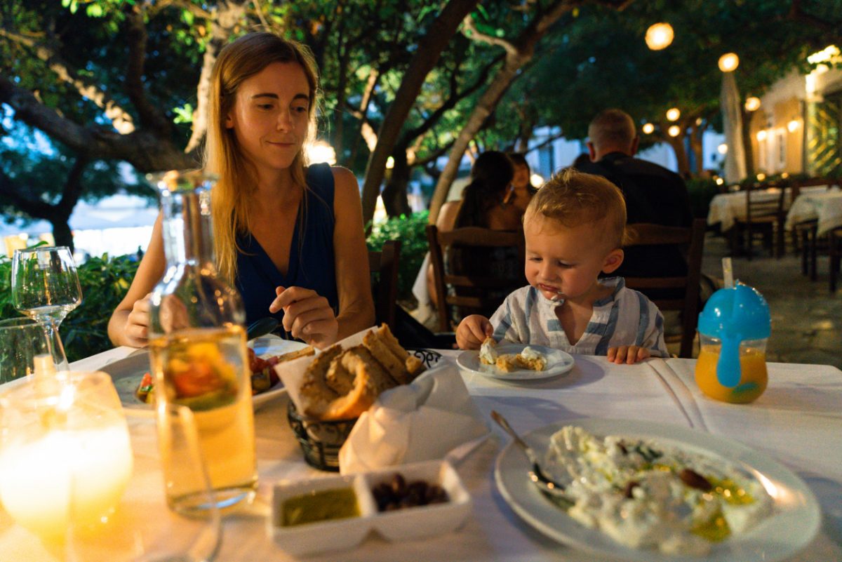 Mother and toddler enjoying a traditional Greek meal outdoors, a delightful experience when traveling in Greece with a baby.
