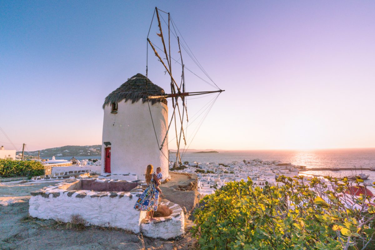 Woman and child admiring a traditional Greek windmill at sunset, a tranquil family moment in Greece with a toddler.
