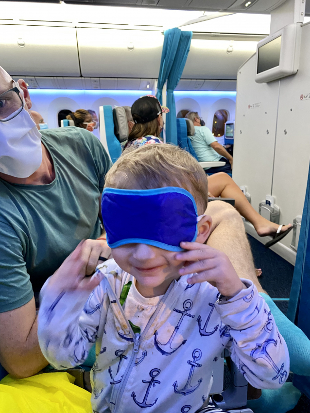 Toddler playing peekaboo with an eye mask on an airplane, a cute and fun way to keep him entertained while flying.
