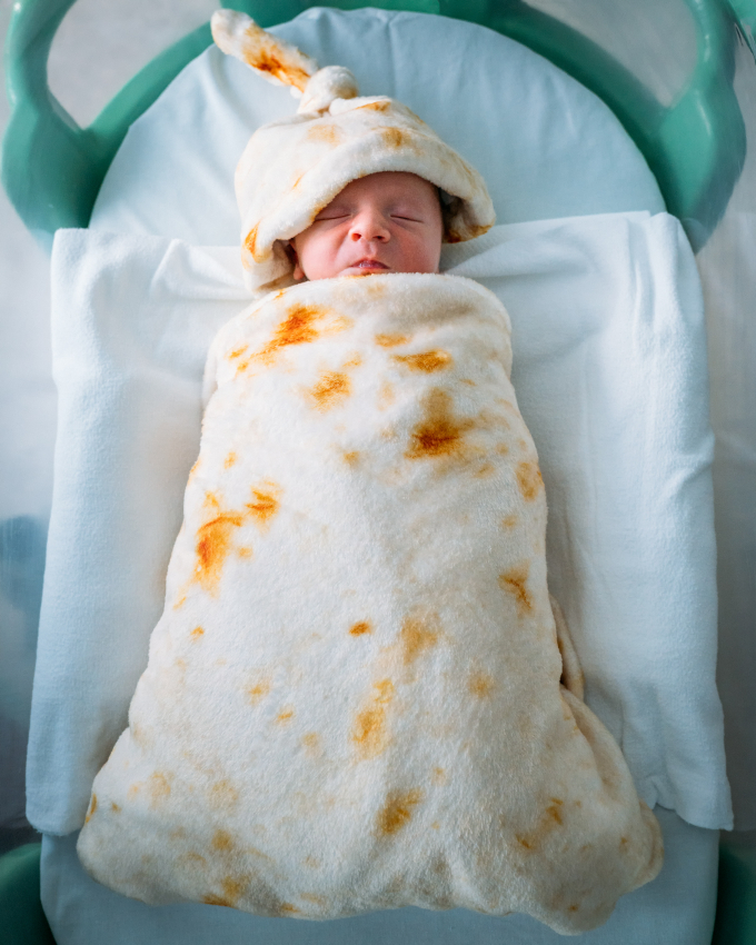 Newborn baby wrapped in a tortilla blanket, a cute representation of the joy of giving birth in Mexico.
