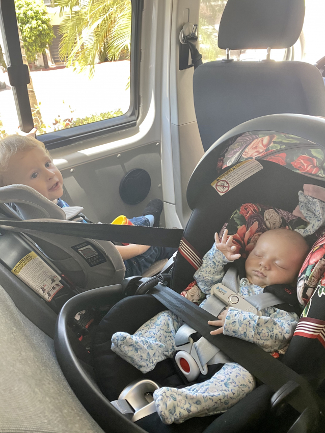 Curious toddler looking at his newborn sibling asleep in a car seat, family moments after giving birth in Mexico.
