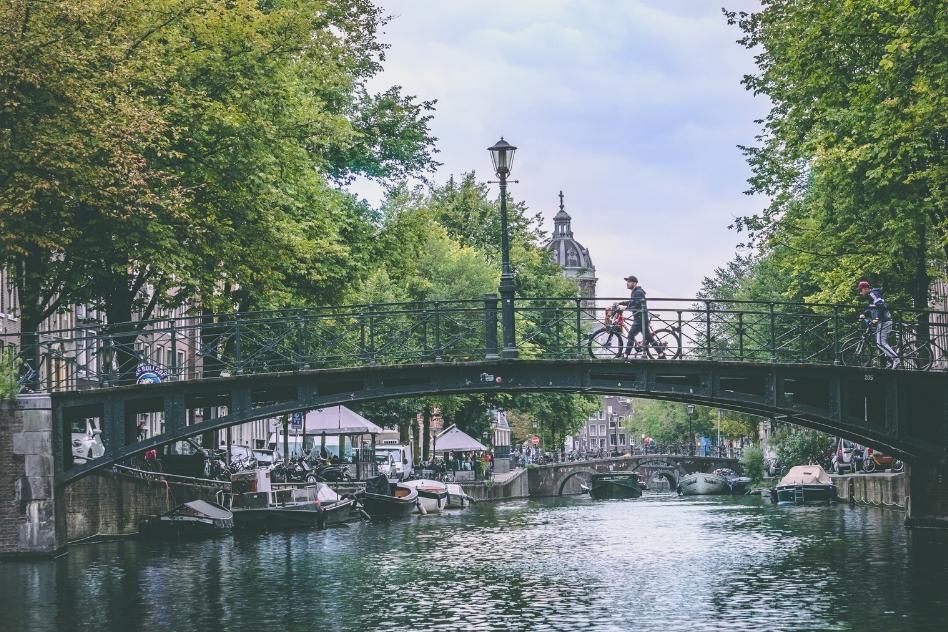 Cyclists crossing a picturesque bridge over Amsterdam's serene canals, a must-see during your 2 days in Amsterdam.