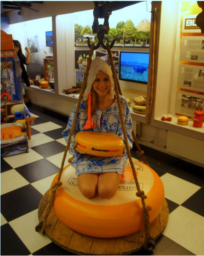 Traveler smiling on a cheese swing at the Amsterdam Cheese Museum, a quirky stop on your Amsterdam itinerary.