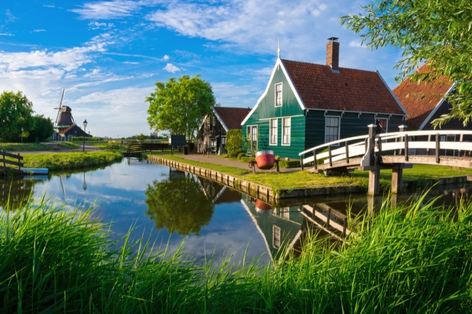 Idyllic view of Zaanse Schans with traditional Dutch windmills and a classic green wooden house reflecting in a tranquil canal, a picturesque scene to include in your Amsterdam itinerary.