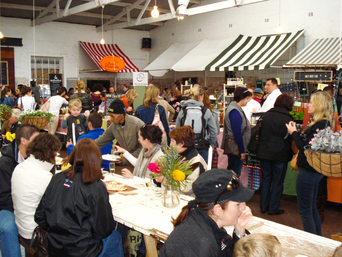 Bustling indoor market in Cape Town, filled with locals and tourists shopping for fresh produce and artisanal goods, a lively spot to experience the city's diverse flavors and crafts.